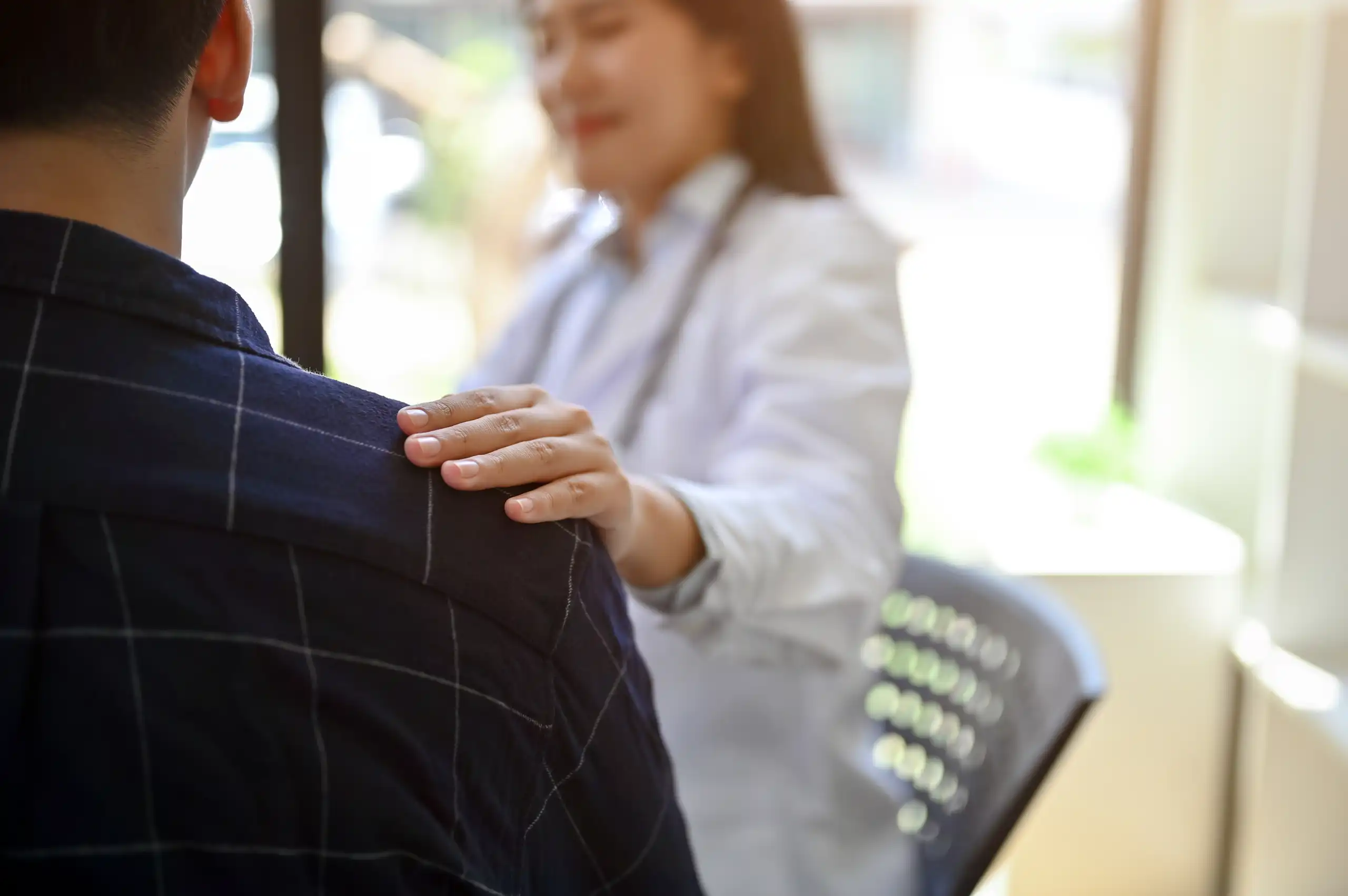 Close up of a doctorโs hand offering comfort by resting on a patientโs shoulder