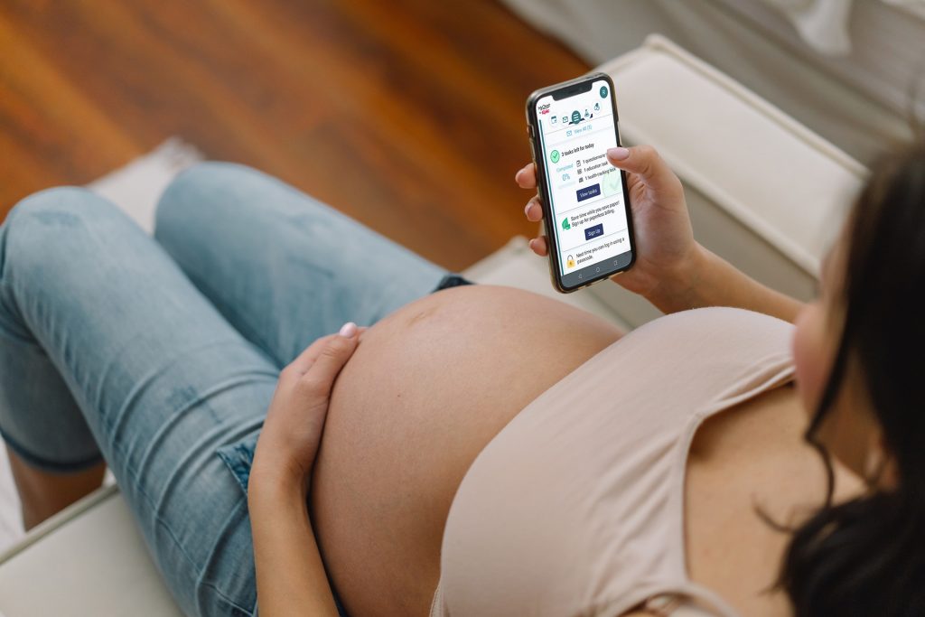 Pregnant woman holding phone with the MyChart Pregnancy Care Companion feature